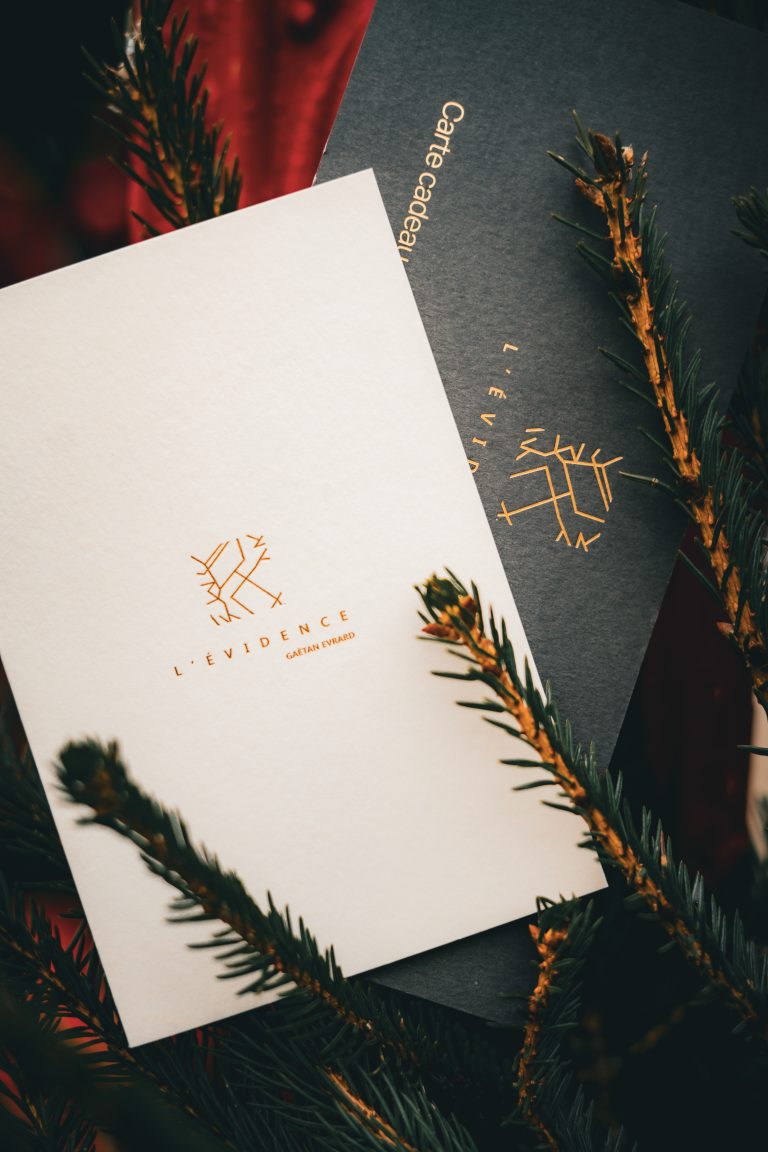 Belle carte cadeau papier L’Évidence parmi des branches de sapin