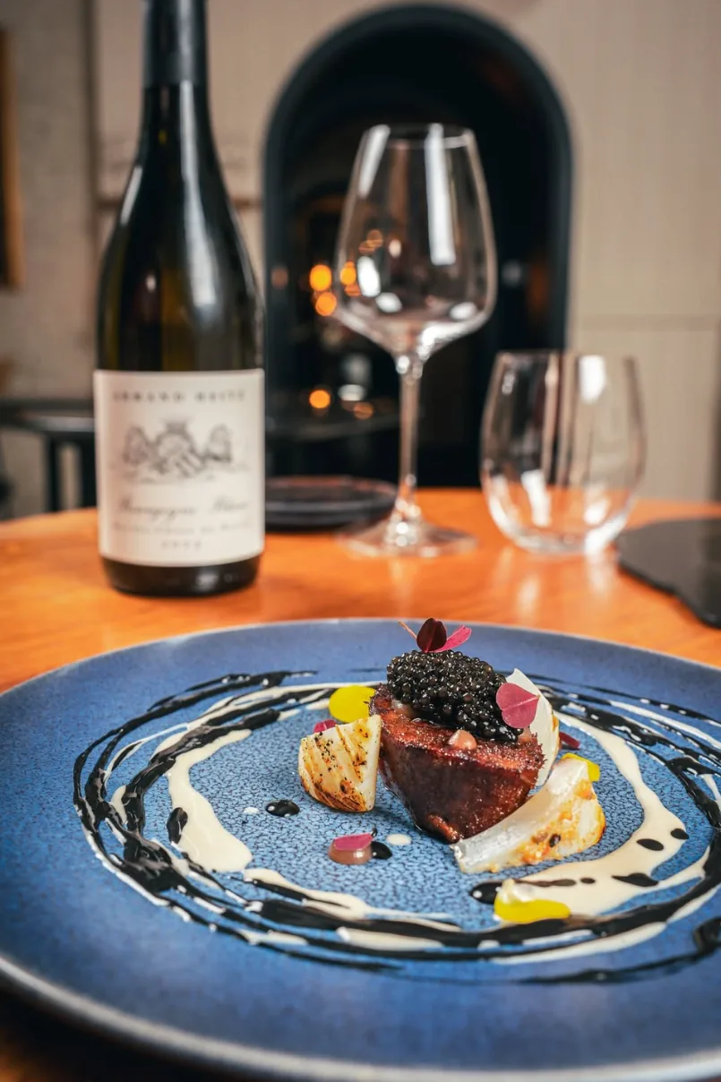 Assiette surmontée de caviar et verre de vin sur une table de L’Évidence